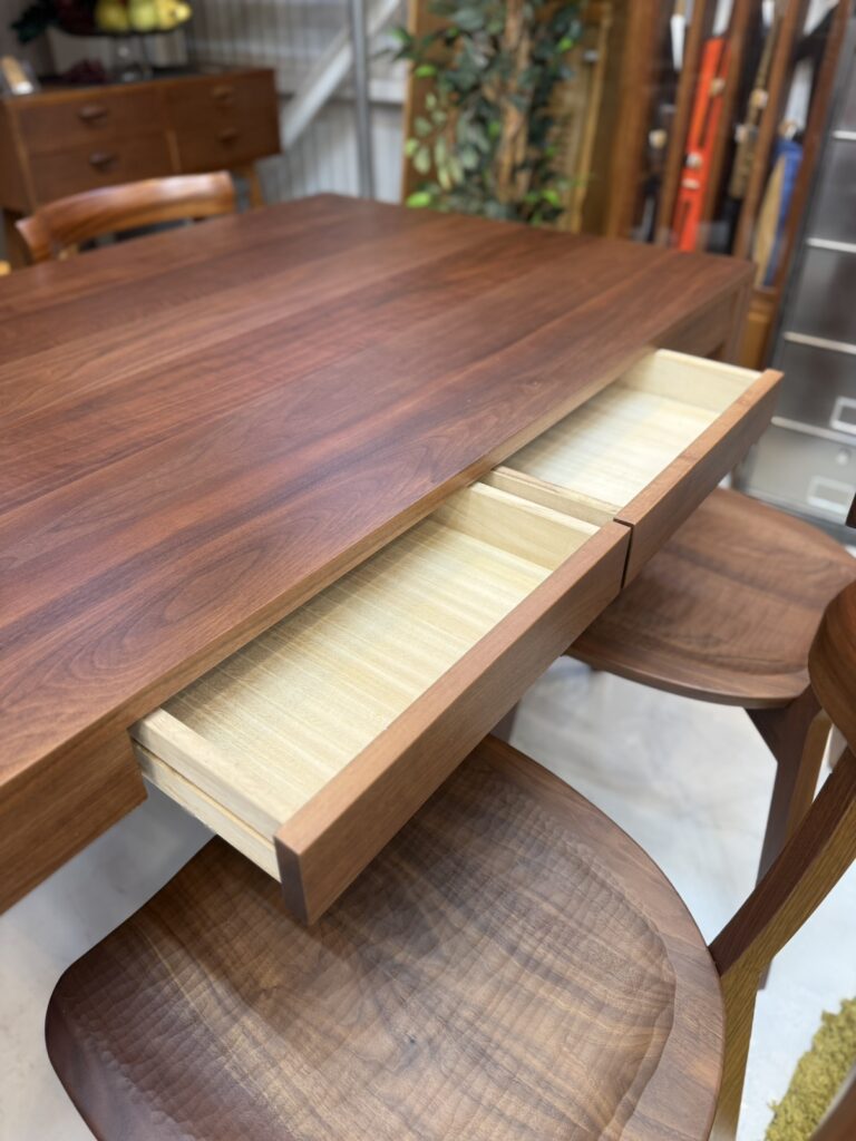 EARLY TIMES α（アーリータイムスアルファ）ウォルナットダイニング150cmダイニングチェア5点セット ダイニング用 天板下に設けられた引き出しが実用性とデザイン性を両立。カトラリーやリモコン、小物をすっきり収納でき、生活感を抑えた美しいダイニング空間を実現。ウォルナットの上質な質感と一体化したシンプルな構造で、旭川家具らしい丁寧な造りが際立つ。